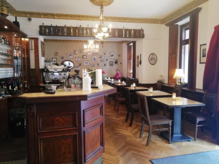 A photo of the inside of a restaurant with a bar on the left and tables and chairs on the right.