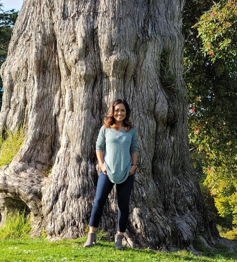 A photo of Ny Nourn standing in front of a large tree.