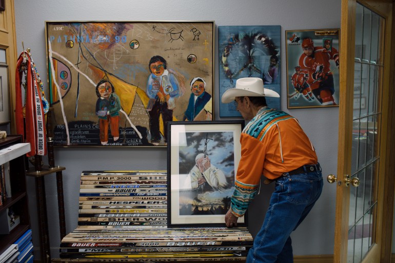 A photo of Chief Willie Littlechild in his office with paintings and he is holding a framed photo.