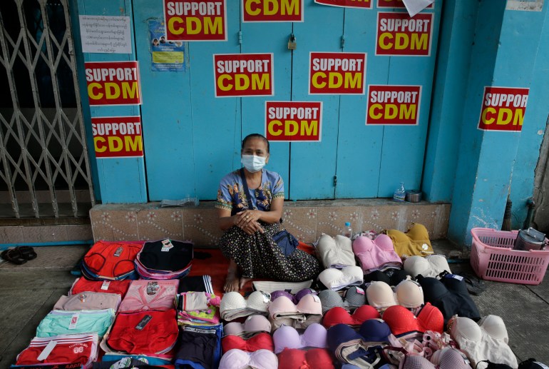 A woman sits behind her stall selling underwear on the street in Yangon in front of posters calling for mass civil disobedience