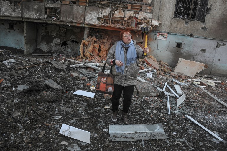 A woman poses for a photo next to a damaged building in the aftermath of a shelling in Kharkiv