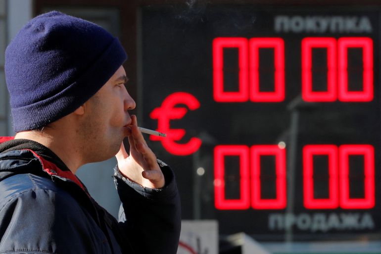 A man smokes as he walks past a currency exchange office in Saint Petersburg, Russia