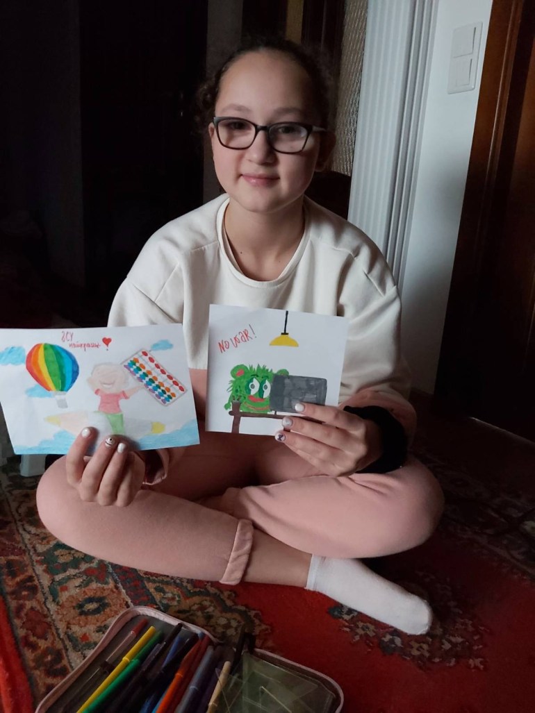 11-year-old Samira holds up 2 drawnings