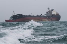 A police fire boat (L) is seen next to an oil tanker tilting to one side after it caught fire off the coast
