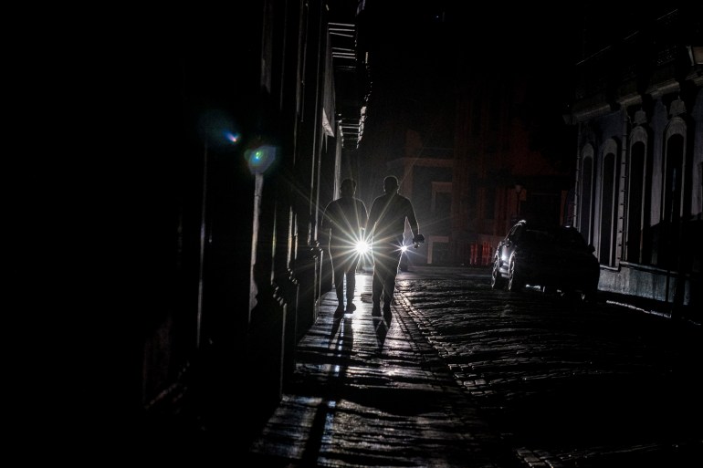 A cars headlights are seen past people walking on a dark in San Juan, Puerto Rico 