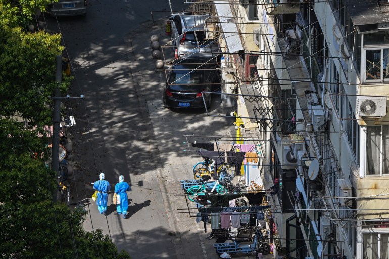 Health workers, wearing personal protective equipment (PPE), walk on a street in a neighborhood during a COVID-19 lockdown in Shanghai's deserted Jing'an district
