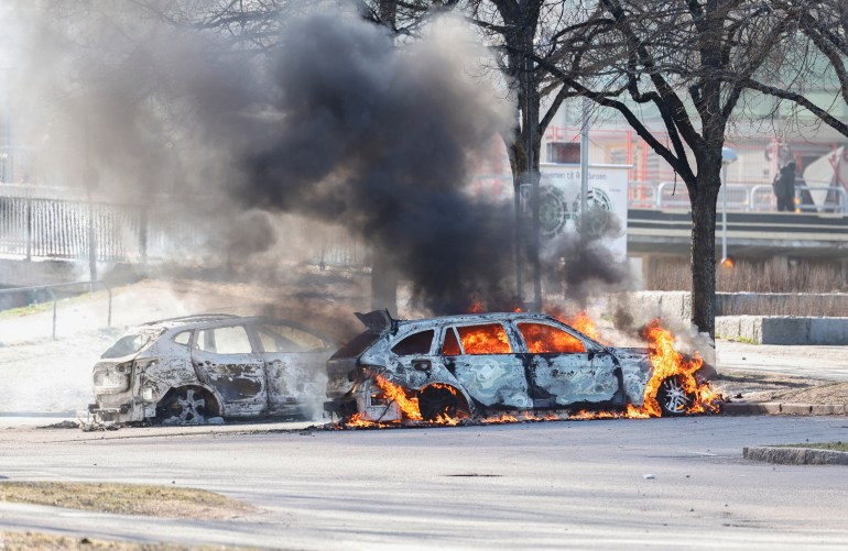 Two cars are burning in a parking lot during rioting in Norrkoping, Sweden