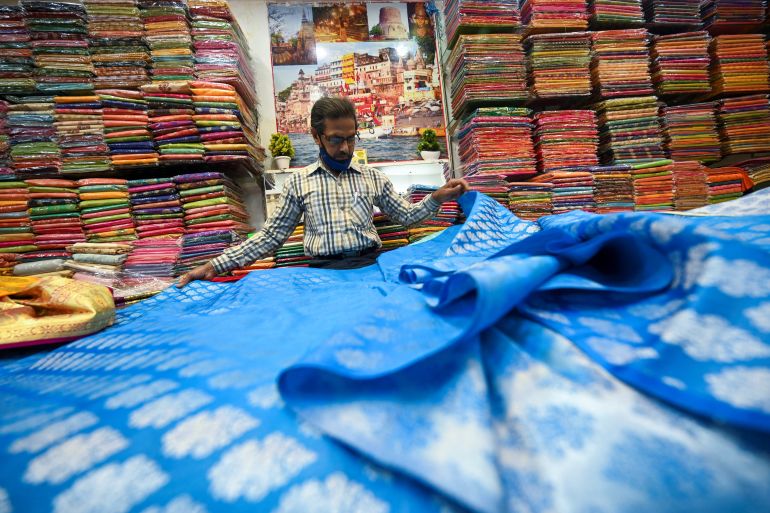 a shopkeeper shows a traditional Banarasi sari at a store in Varanasi, India