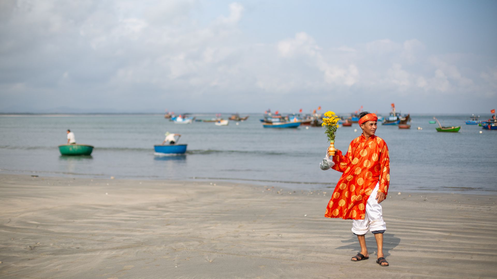 A photo of a whale worshipper dressed in a red-and-crimson áo dài holding flowers on the beach.