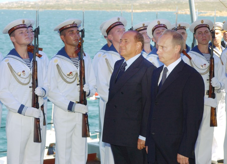 Silvio Berlusconi walks with Vladimir Putin next to an honour guard of sailors on the Moskva in Sardinia in 2003