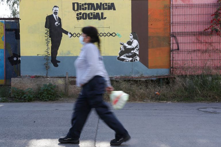 A woman walks by graffiti that reads, 'Social distance' in Santiago, Chile