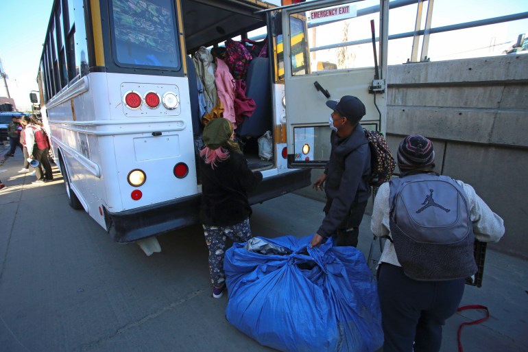 Migrants carry their belongings to a bus