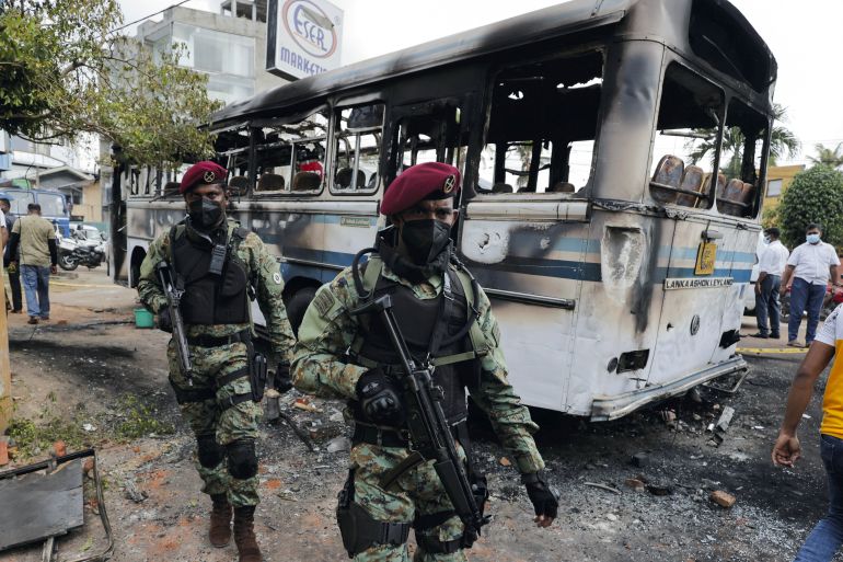 Sri Lankan army commandos walk past a damaged bus after it was set on fire by demonstrators