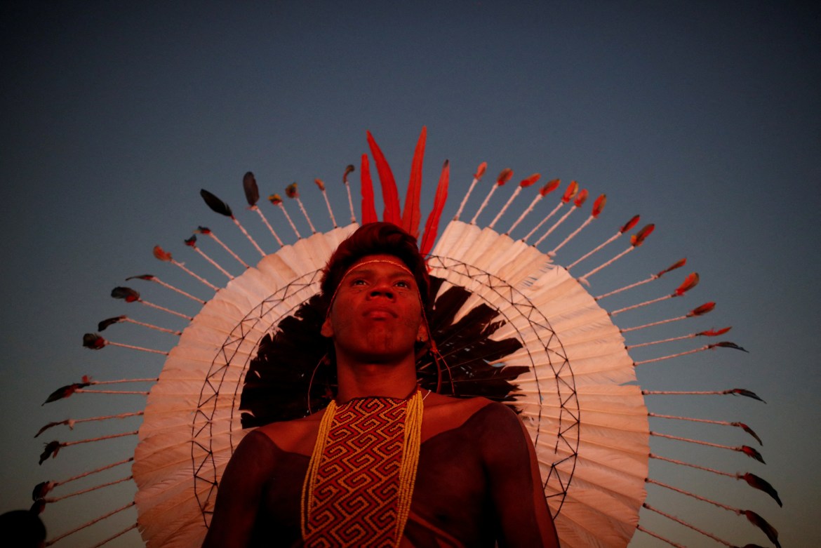 The sun illuminates an Indigenous man as it sets and he looks on during a protest