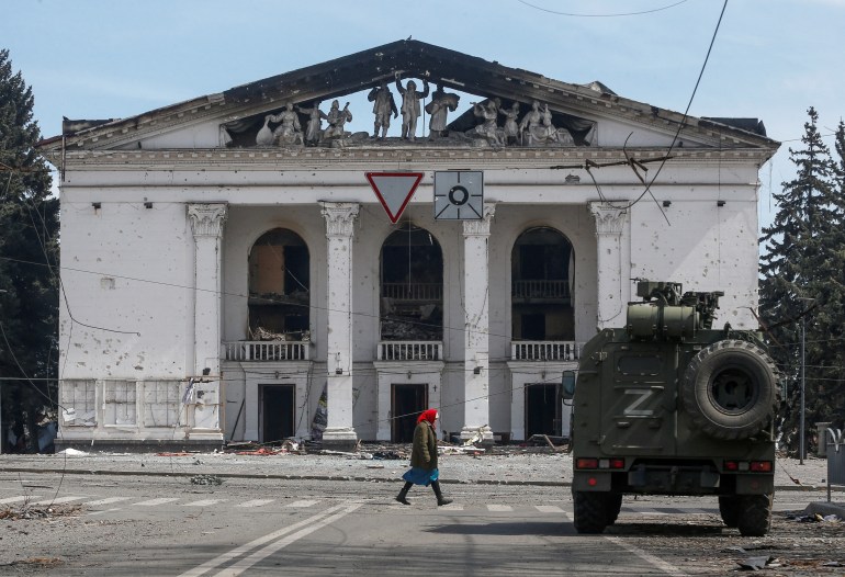 A woman walks next to an armoured vehicle of pro-Russian troops the building of a theatre destroyed in the course of Ukraine-Russia conflict in the southern port city of Mariupol, Ukraine 