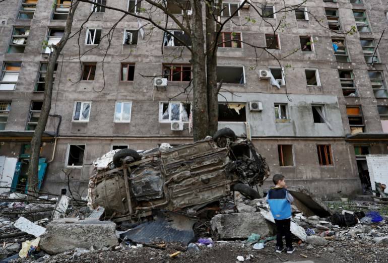 A boy stands next to a wrecked vehicle in front of an apartment building damaged during Ukraine-Russia conflict in the southern port city of Mariupol, Ukraine