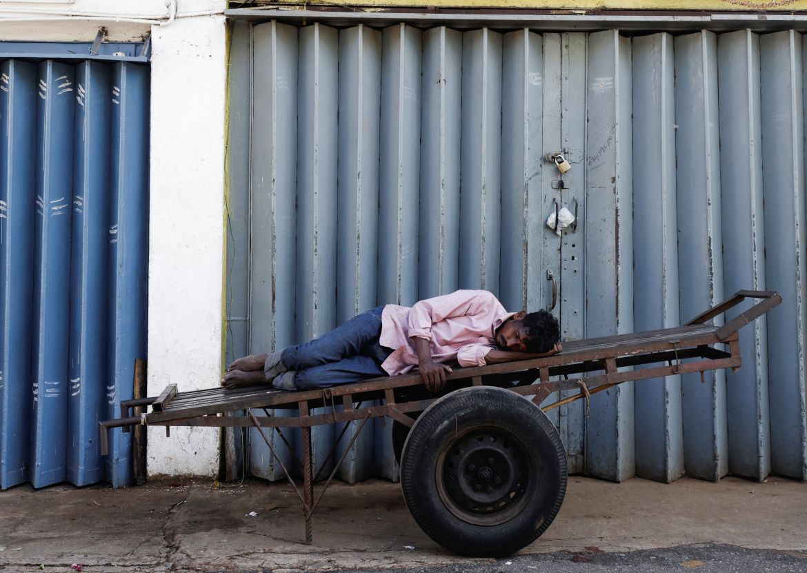 A worker sleeps on a cart in front of a closed essential food store