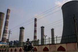A motorcyclist drives past chimneys and a cooling tower at a coal-fired plant in Andhra Pradesh, India