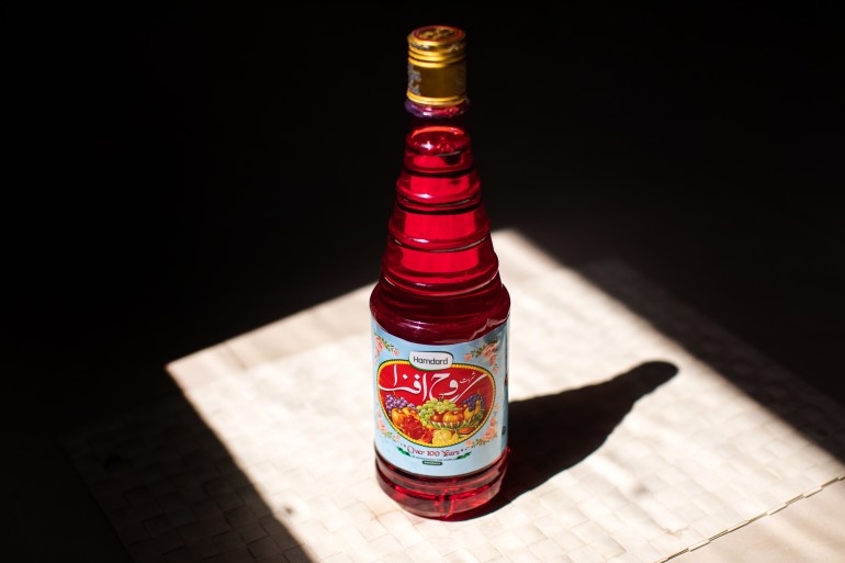 A bottle of rooh afza is shown on a straw mat, in a square of sunlight