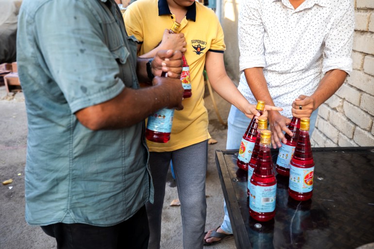 A photo of three men grabbing as many bottles of rooh afza as they can fit in their arms at a charitable food distribution site