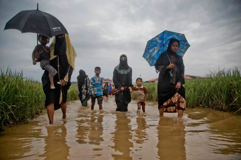 Rohingya women holding umbrellas wade through a chocolate-brown coloured channel after fleeing Myanmar in 2017.