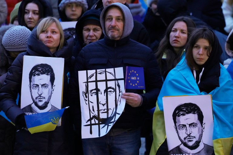 People hold portraits of Ukrainian President Volodymyr Zelenskyy and Russian President Vladimir Putin, center, during an anti-war rally in front of the Palace of Culture and Science in Warsaw