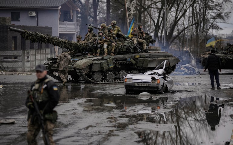 A man stands next to a civilian vehicle that was destroyed during fighting between Ukrainian and Russian forces that still contains the dead body of the driver 