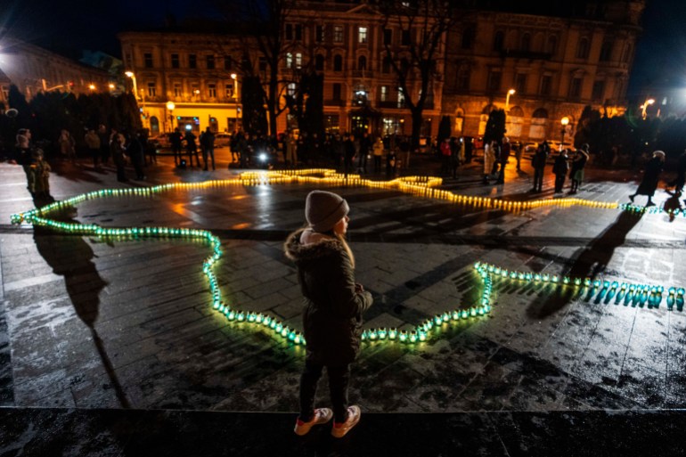 A girl stands in front of lit candles forming the shape of Ukraine's map, in memory of lost lives, in front of the Taras Shevchenko monument, in Lviv, western Ukrain