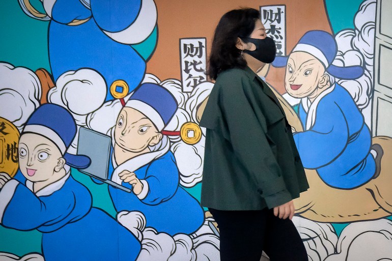 A woman wearing a face mask walks past a mural of healthcare workers in blue medical gowns in Beijing.