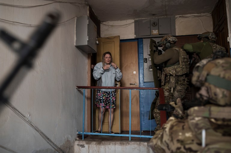 An alarmed looking woman looks as Security Service of Ukraine (SBU) service members come up the stairs of her building during an operation to arrest suspected Russian collaborators in Kharkiv.