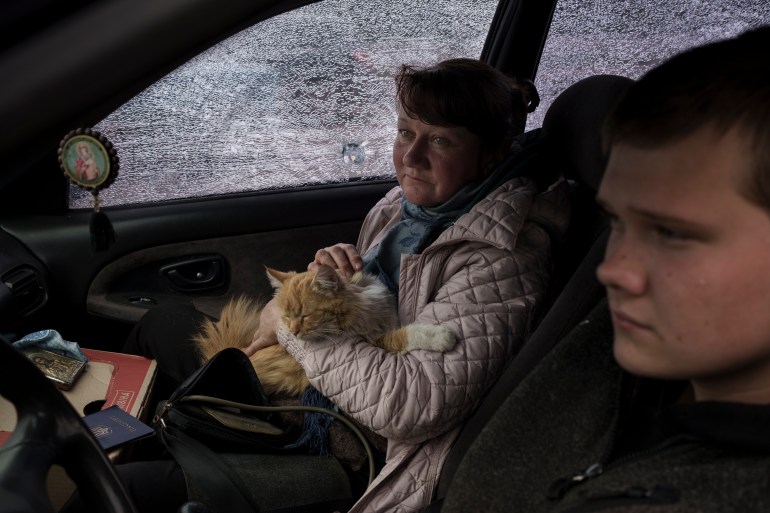A woman sits in a car with her ginger cat on her lap next to a window shattered by shrapnel as she arrives in Kharkiv after being evacuated