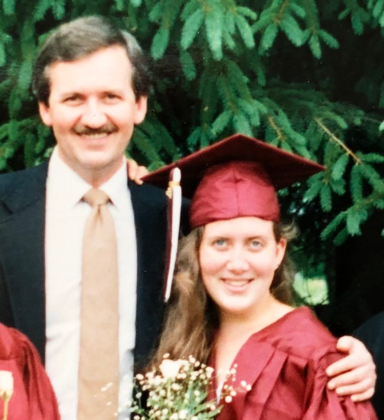 A girl in a graduation cap and gown poses with her uncle