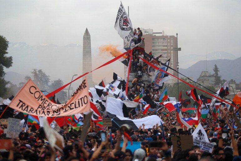 Protesters wave Chilean flags and climb the monument to General Baquedano