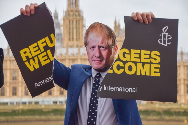 An activist dressed as Boris Johnson holds a torn 'Refugees Welcome' placard during the demonstration.