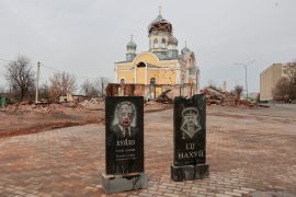 Tombstones with portraits of Russian president Vladimir Putin and Belarus President Alexander Lukashenko are seen in front of a church damaged by shelling