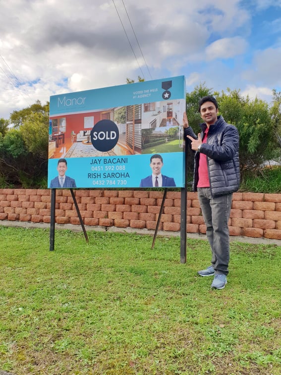 Shravan Nagesh standing next to a real estate sign with the word 'sold' prominently displayed.