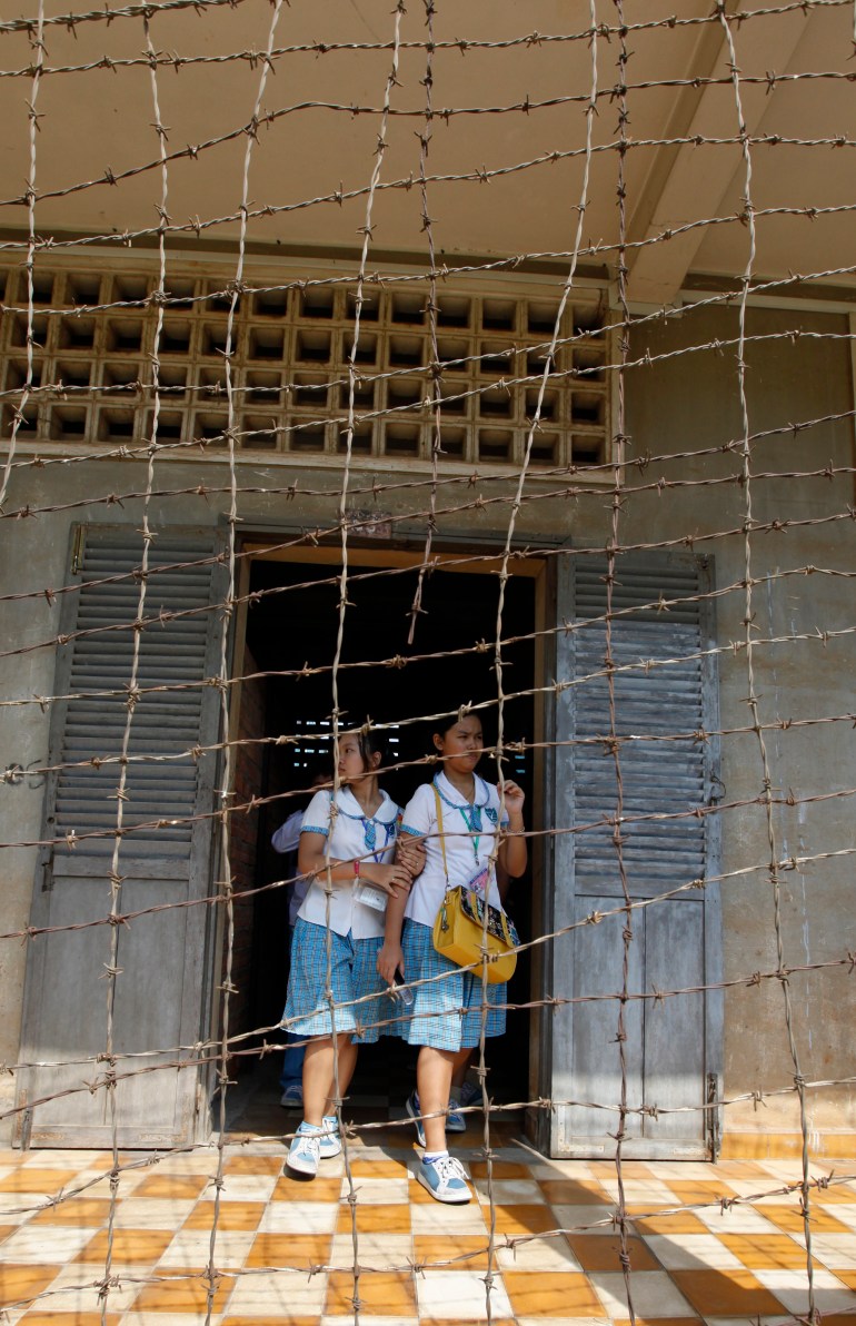 Two female students stand at a door behind rusted barbed wire as they visit the Tuol Sleng Genocide Centre from where the Khmer Rouge sent thousands of Cambodians to their deaths