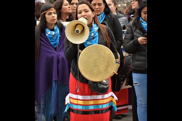 A photo of Sarah Eagle Heart using a bullhorn with a crowd of people behind her.