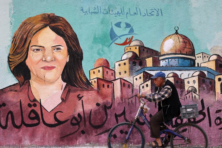 A Palestinian man rides his bicycle in front of a mural painted by an artist in honour of slain veteran Al-Jazeera journalist Shireen Abu Akleh, in Gaza City on May 13, 2022. - Abu Akleh, who was shot dead on May 11, 2022 while covering a raid in the Israeli-occupied West Bank, was among Arab media's most prominent figures and widely hailed for her bravery and professionalism.