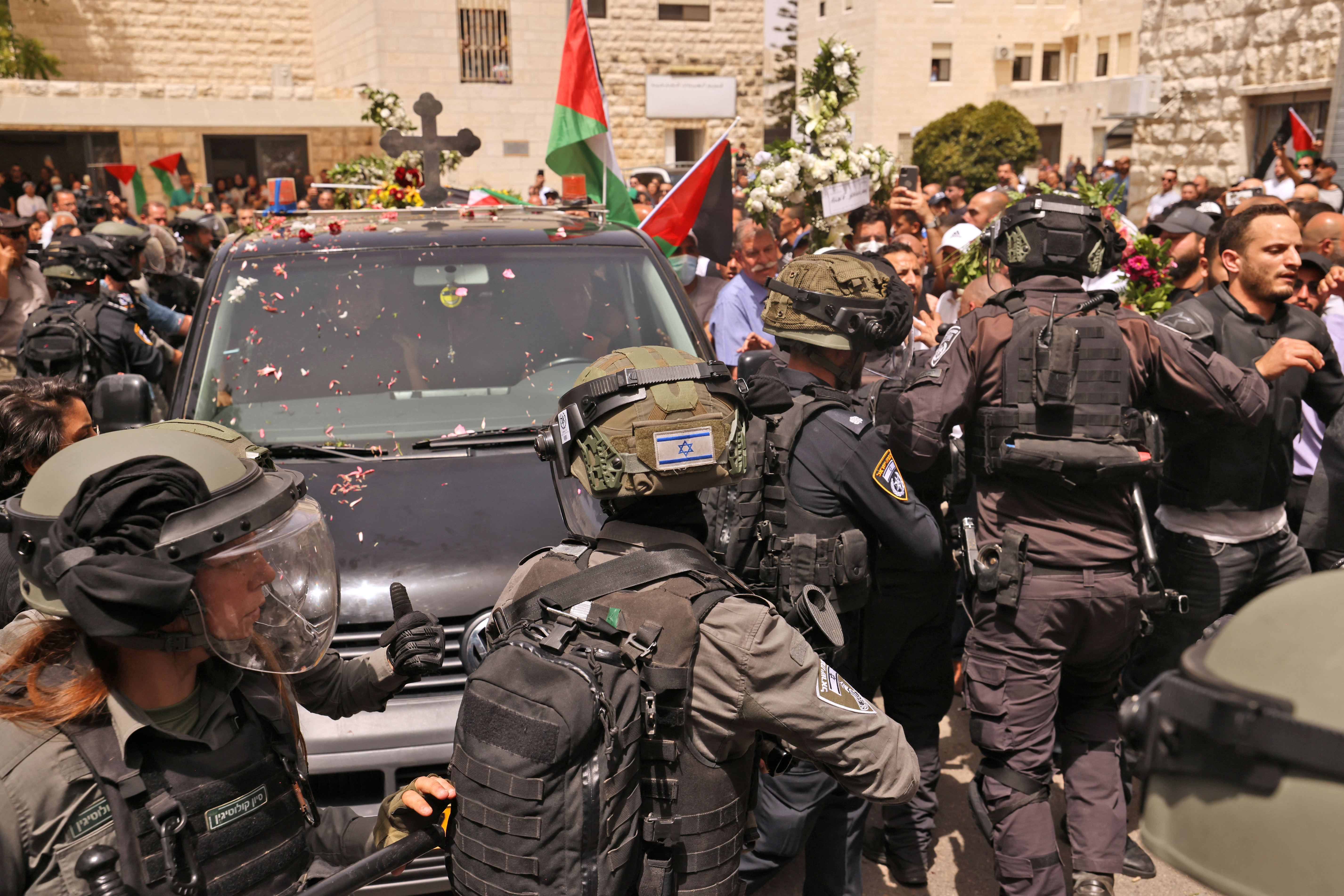 Israeli security forces surround a vehicle carrying the casket of slain Al-Jazeera journalist Shireen Abu Akle out of a hospital, as Palestinian mourners toss rose petals, before being transported to a church and then her resting place, in Jerusalem, on May 13, 2022. - Abu Akleh, who was shot dead on May 11, 2022 while covering a raid in the Israeli-occupied West Bank, was among Arab media's most prominent figures and widely hailed for her bravery and professionalism. (Photo by AHMAD GHARABLI / AFP)
