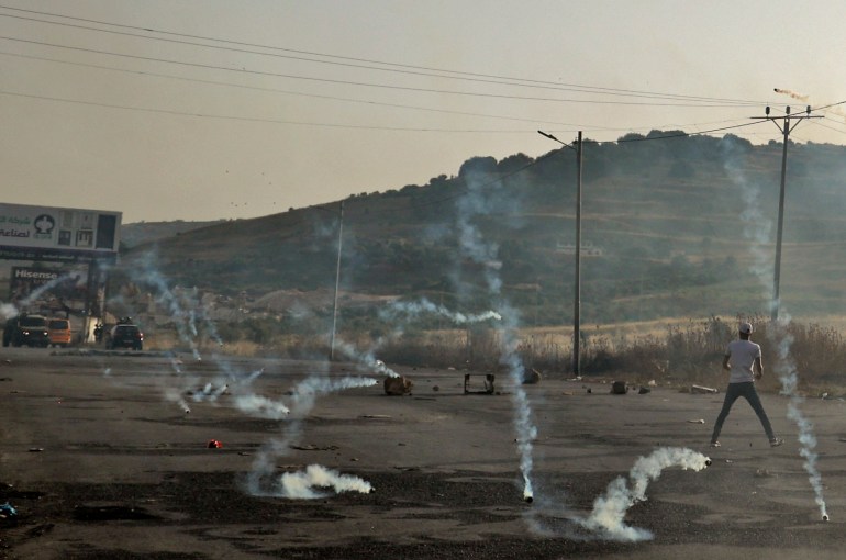 Tear gas canisters fired by Israeli forces fall amidst Palestinian protesters during clashes following a demonstration to denounce the annual nationalist "flag march" through Jerusalem, at the Israeli-controlled Hawara checkpoint near Nablus in the occupied West Bank