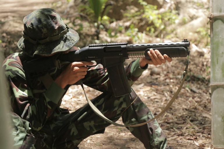 An anti-coup activist in military fatigues kneels on the ground and prepares his rifle to shoot during basic weapons training