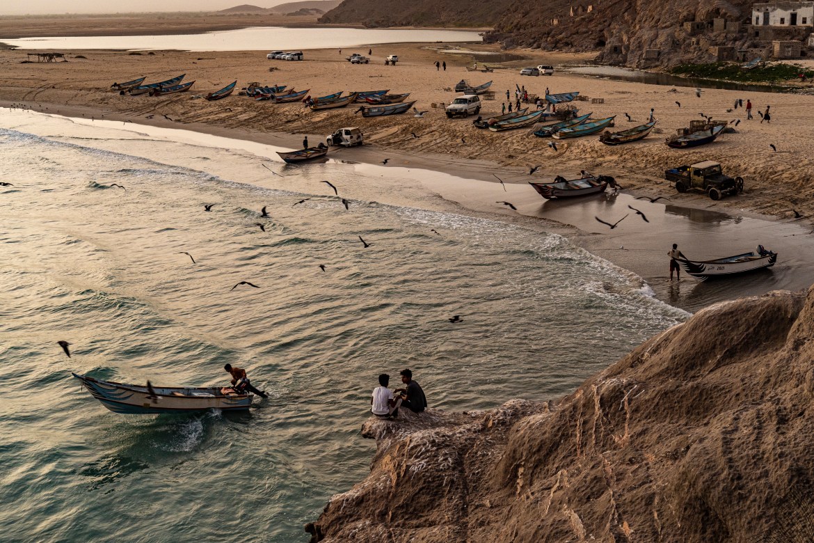 Two boys perched on a cliff watch the fishing boats leave from Khyseet village, near Haswayn