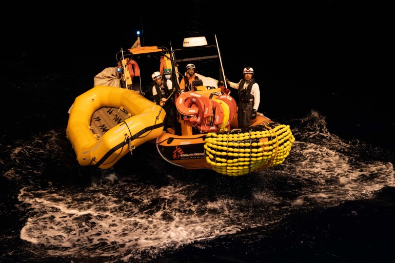 A photo of a boat with a search and rescue team with an empty lifeboat tied to the boat in dark waters.