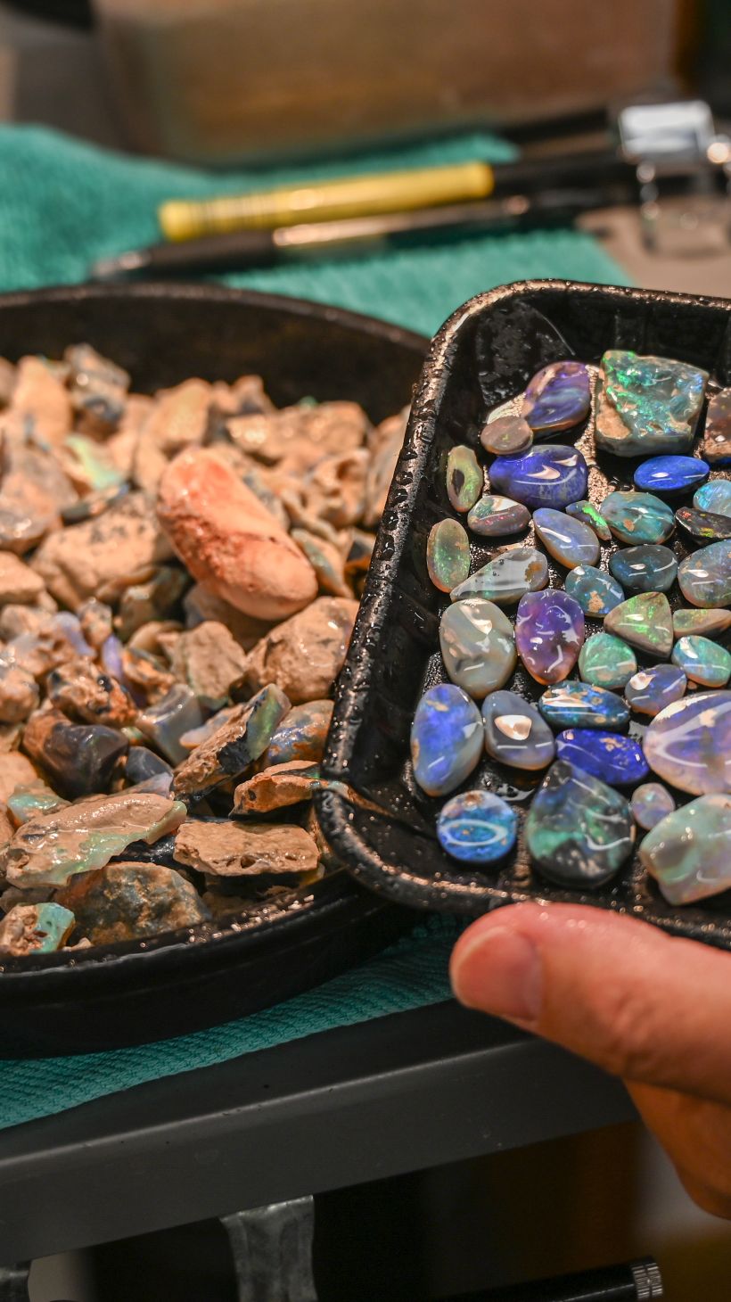 A photo of two plates, one with rubbed back opals, which are blue or green, and the other with rough opals that have been sprayed with water.