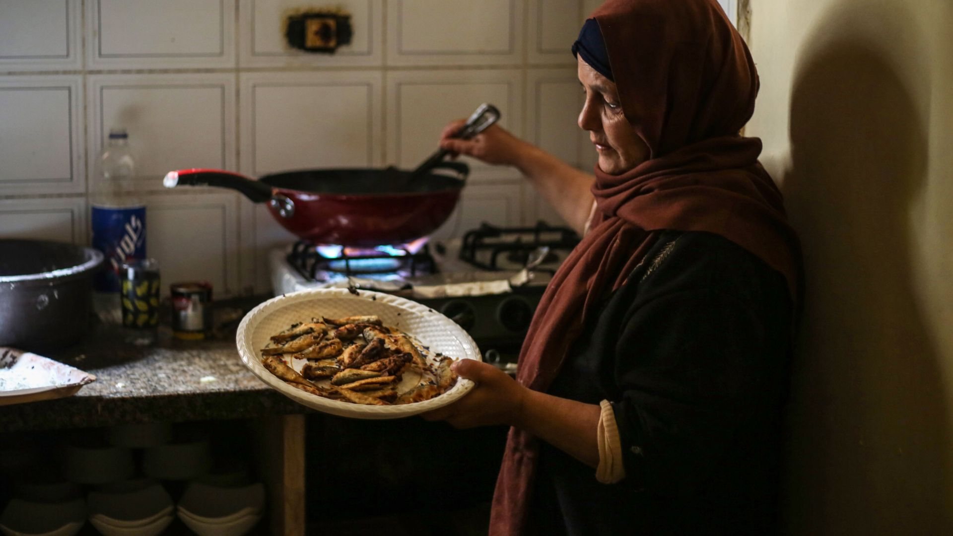Khadr's mother stands by the stove lifting hot, freshly fried sardines out of a wok and onto a plate