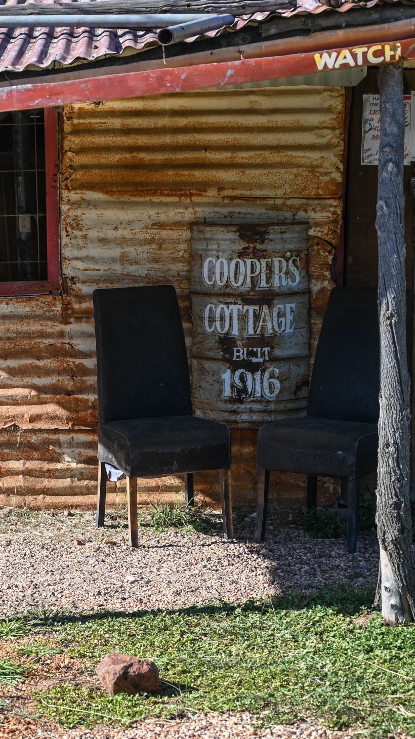 A photo of Coopers Cottage with a sign next to a chair that says "Coopers Cottage 1916".