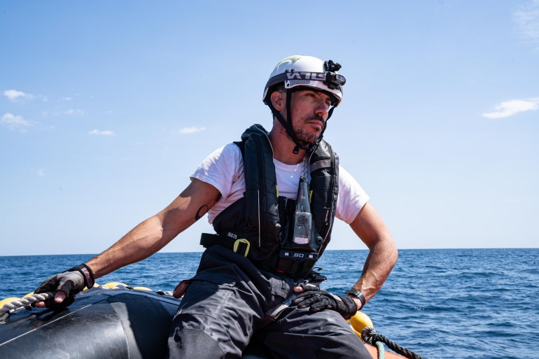 A photo of a man wearing a helmet and a life jacket on a boat in the sea during the day.