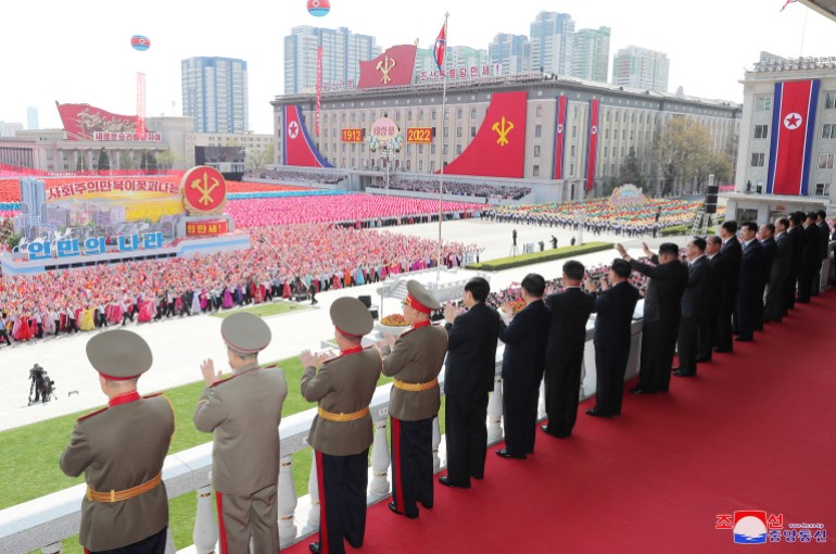 officials in miitary uniform line up on a balcony to watch the massive crowd in Kim Il Sung Square
