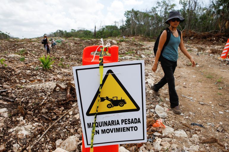 An activist passes by a sign reading "heavy machinery in movement" at one of the construction sections of the Mayan train.
